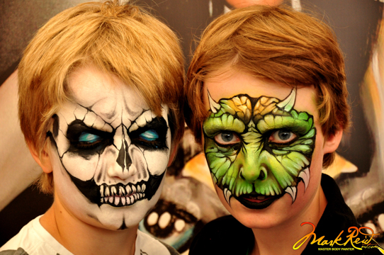 two young people with full face paint one a skull with blue eyes and the other a lizzard with horns